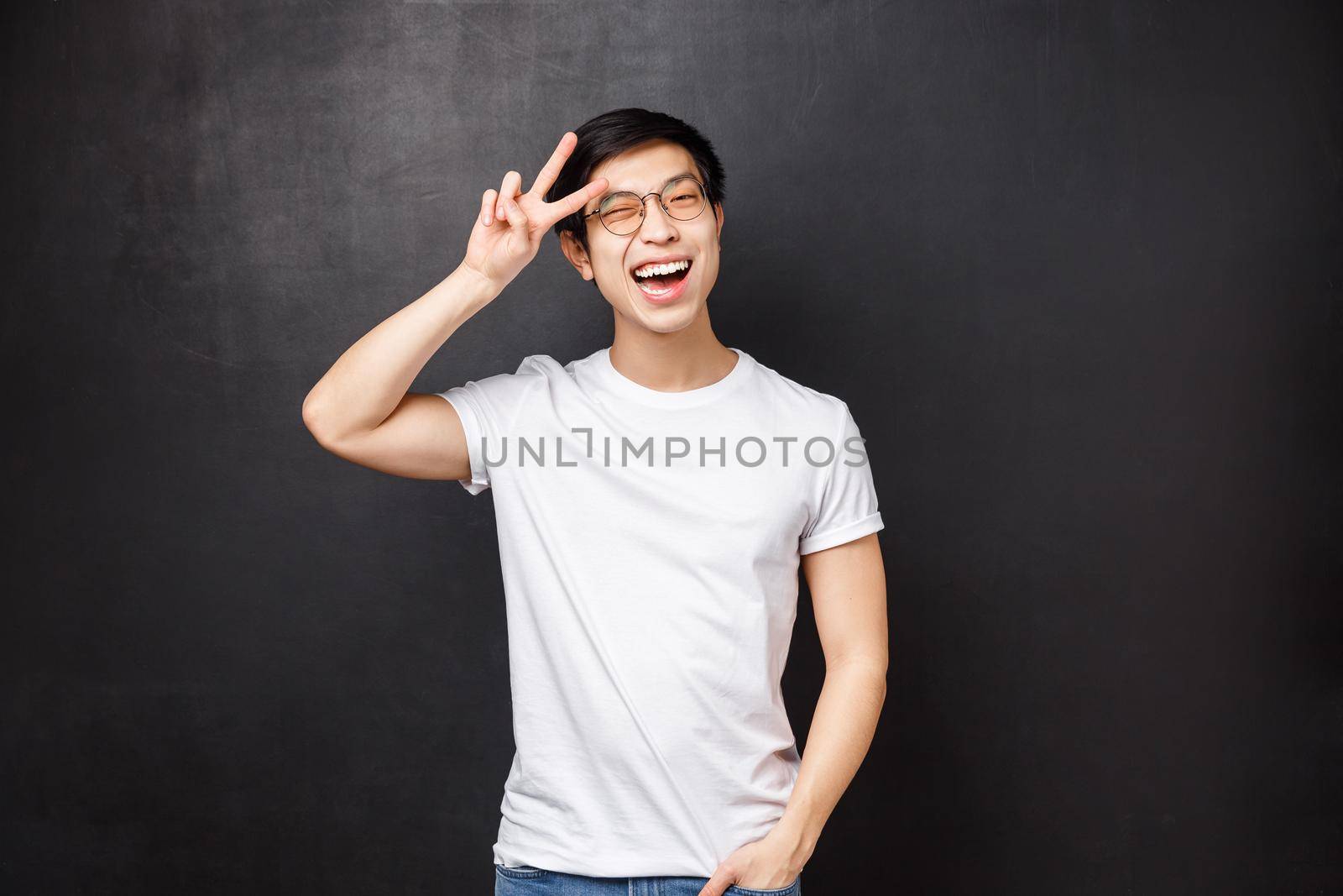 Lifestyle and people concept. Upbeat charismatic asian male model in white t-shirt and sunglasses express positivity and happiness, wink cheeky camera show peace sign near forehead, act kawaii.