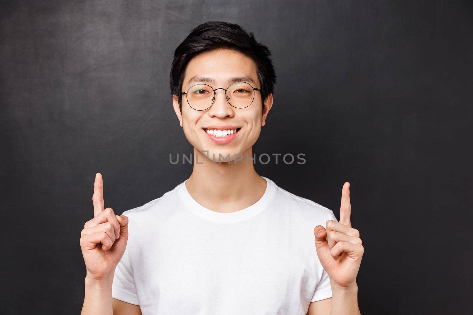 Close-up portrait of successful pleased young asian male entrepreneur, pointing fingers up and looking camera with satisfied beaming smile, talking about how to earn money, black background by Benzoix