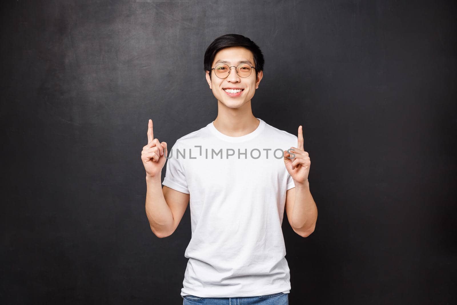 Portrait of joyful handsome smiling asian hipster guy in white shirt and sunglasses, pointing fingers up advice take look, visit this website or read company banner with cool promo, black background by Benzoix