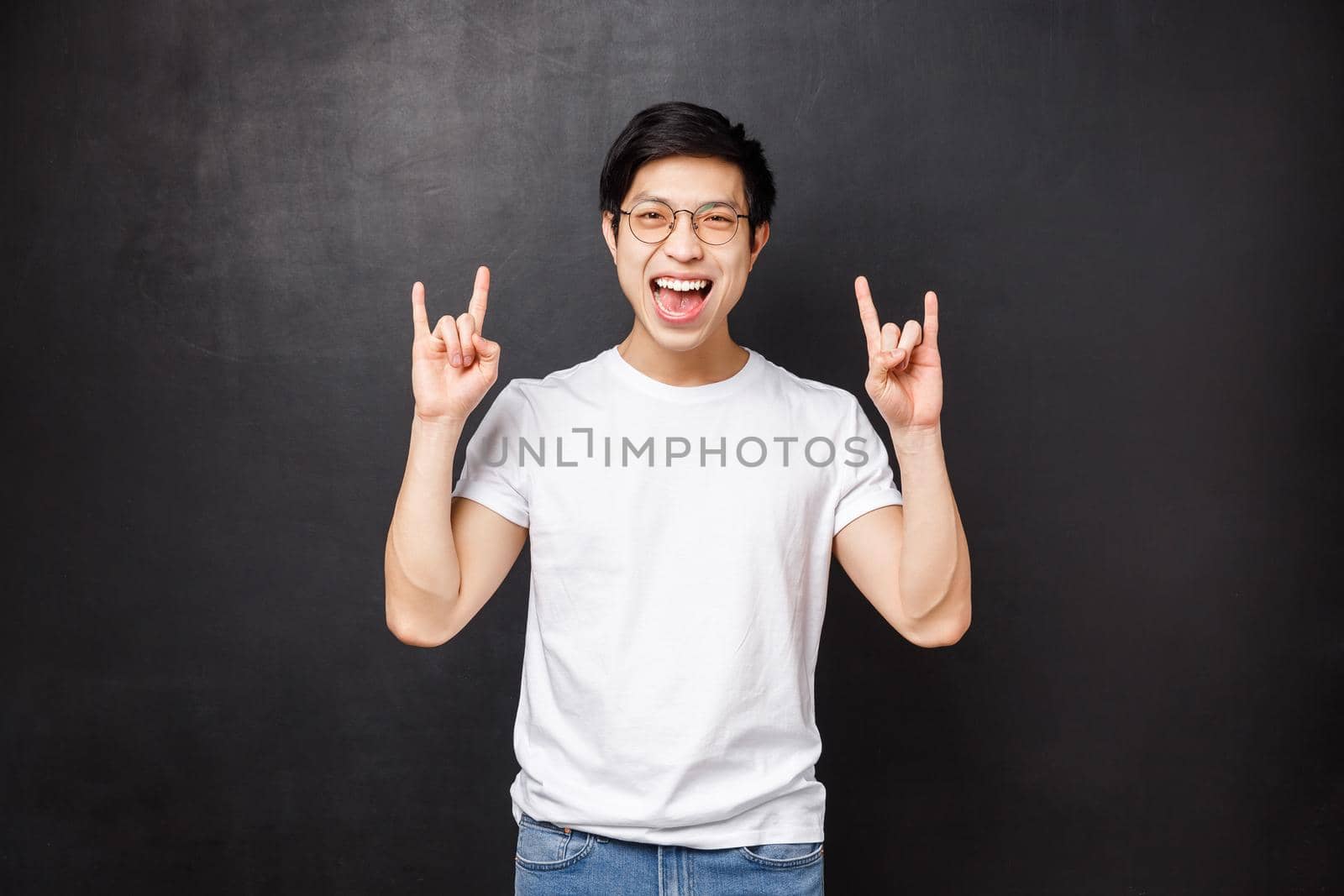 Carefree outgoing young male student having fun at awesome party at dorm, listening cool music at festival, make rock-n-roll gesture smiling and dancing, standing black background.