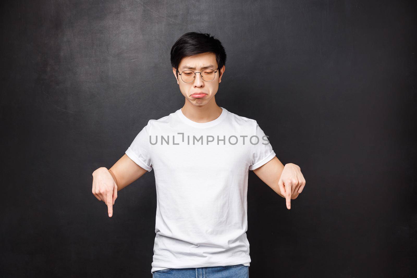 Whining and sobbing miserable upset asian guy feel gloomy, grimacing uneasy and distressed, looking pointing down, losing didnt won prize, regret of missed opportunity, black background.