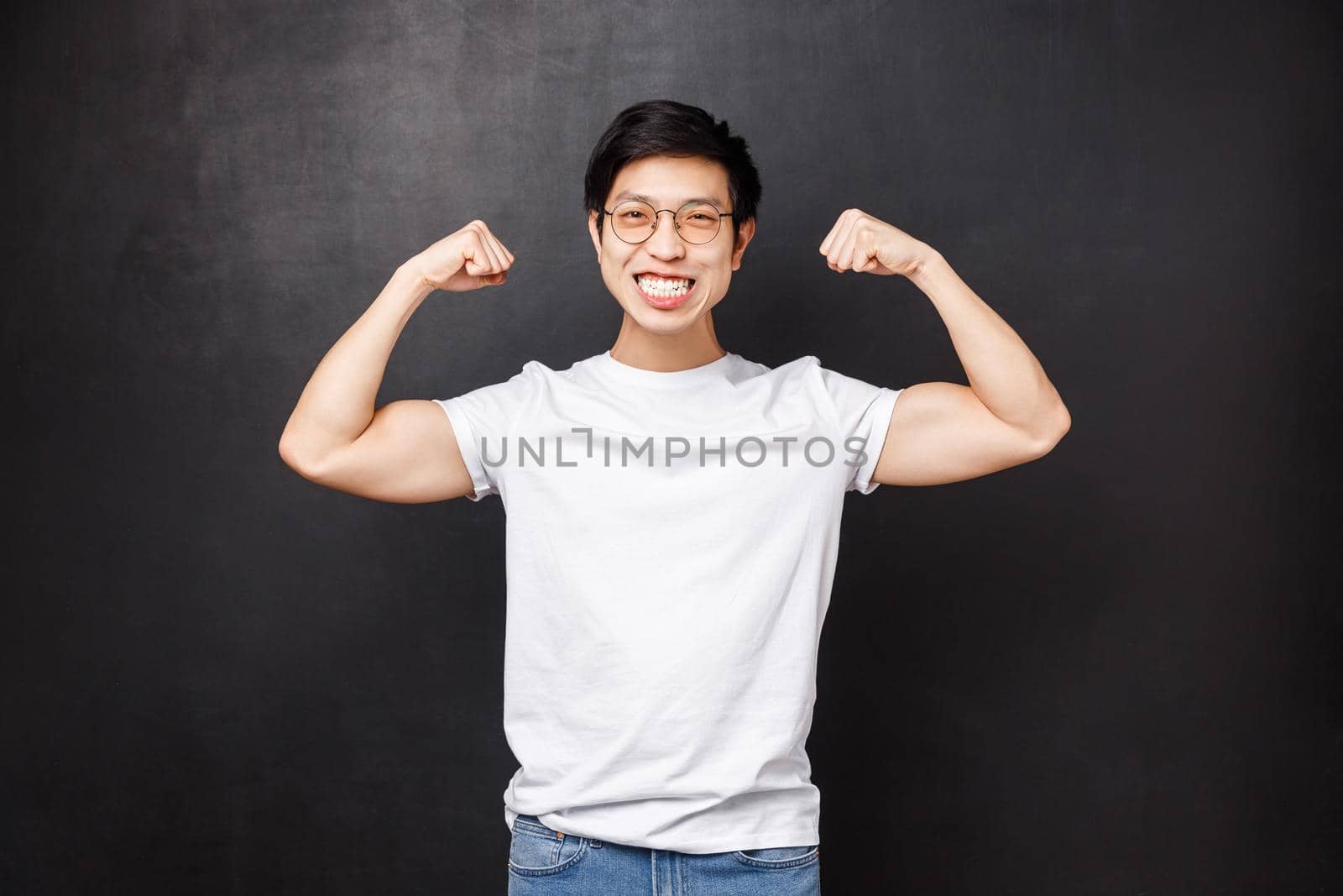 Sport, athletes and olimpics concept. Cheerful and strong young handsome boyfriend bragging with his strength, got fit for summer, flex biceps and smiling satisfied, black background.