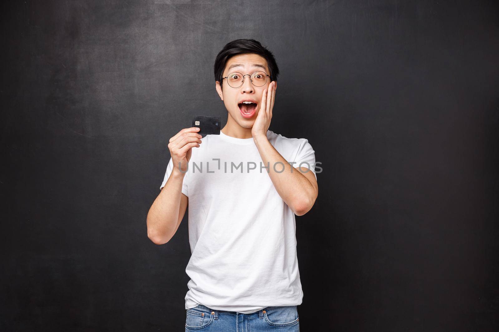 Bank, finance and payment concept. Portrait of excited and amused asian man in t-shirt, open mouth fascinated talking about credit card special features, standing black background intrigued.