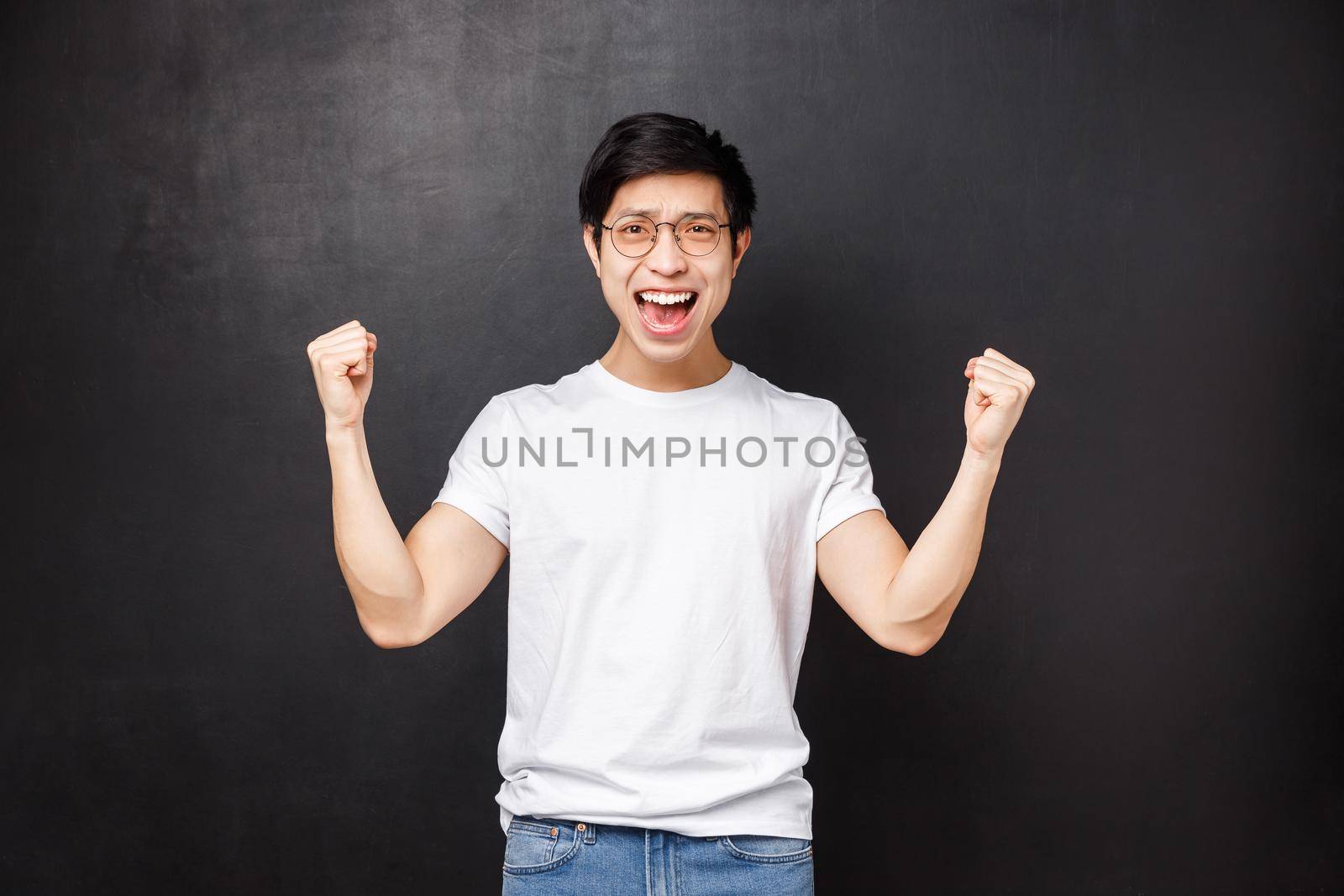 Happy relieved and satisfied young asian guy congratulate his team with win, achieve goal, clench hands like champion, celebrate success saying yes, triumphing over victory, black background by Benzoix