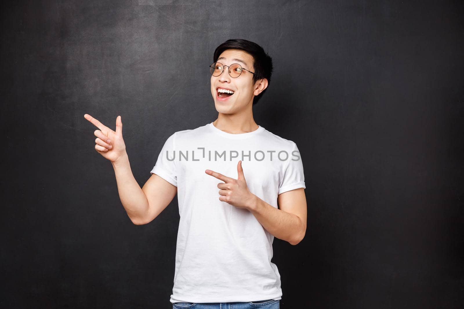 Portrait of enthusiastic and excited handsome chinese guy in white shirt, open mouth amused looking and pointing upper left corner over black background, spot great discounts by Benzoix