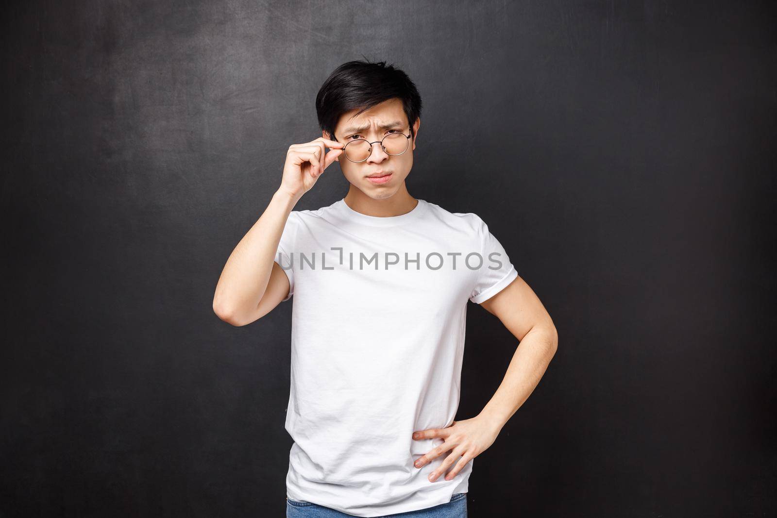 Portrait of frustrated and suspicious young male student have part-time job as tutor, look disbelief and confused at person, fixing glasses on eyes, squinting doubtful, standing black background by Benzoix