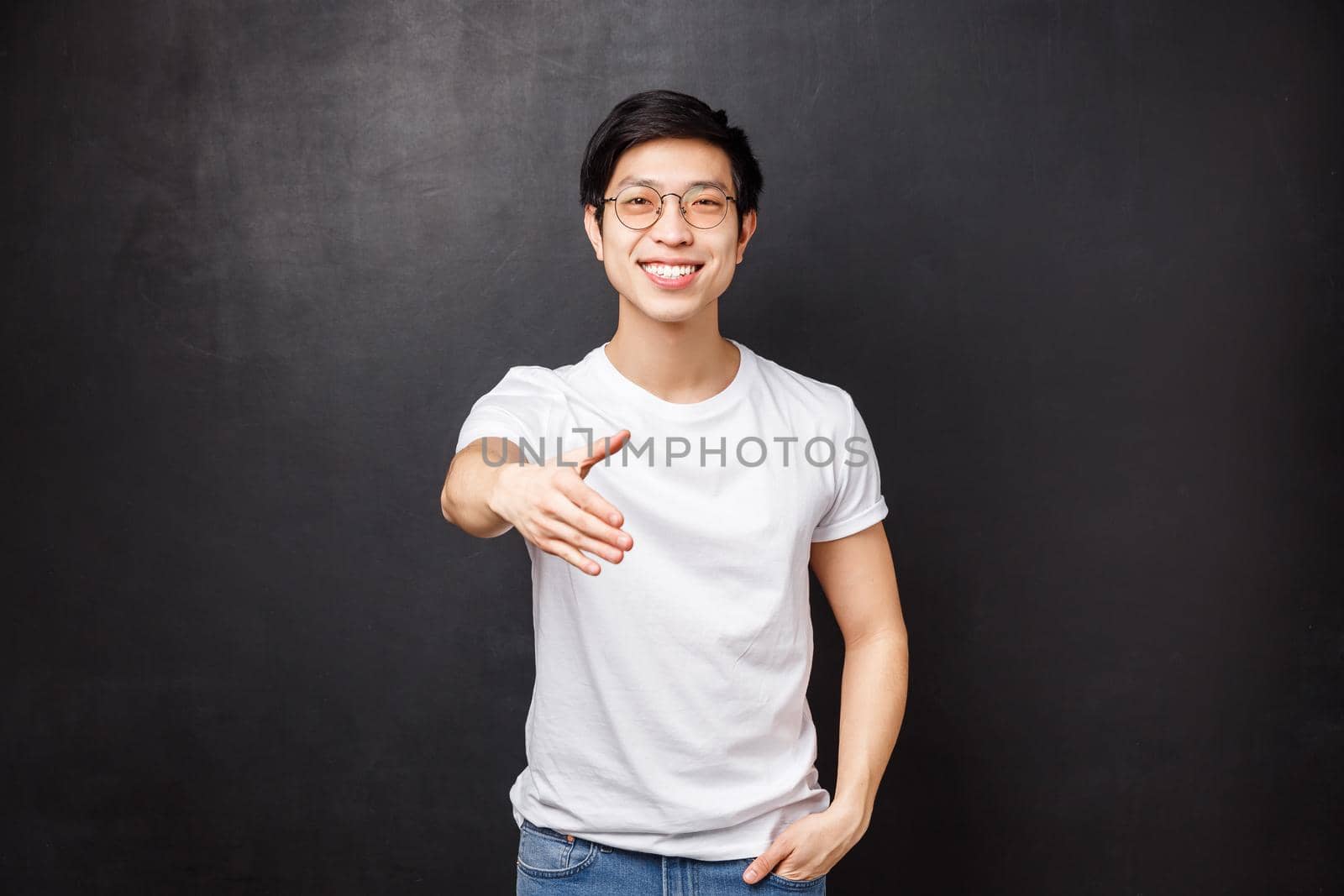 Nice to meet you. Pleasant friendly young stylish asian man in glasses and t-shirt, extend hand for handshake smiling, meeting new person, get to know team members, say hello, black background.