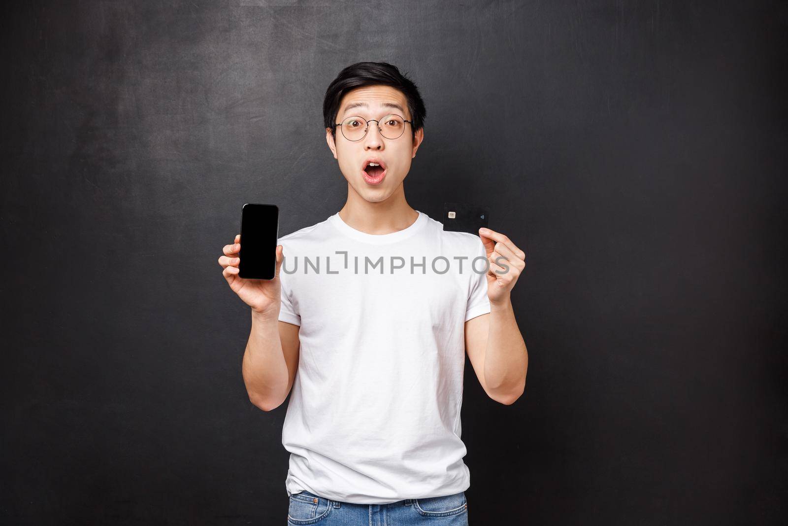 Bank, finance and payment concept. Impressed overwhelmed young asian man promote credit card service features, banking application, show his account on mobile screen, black background by Benzoix