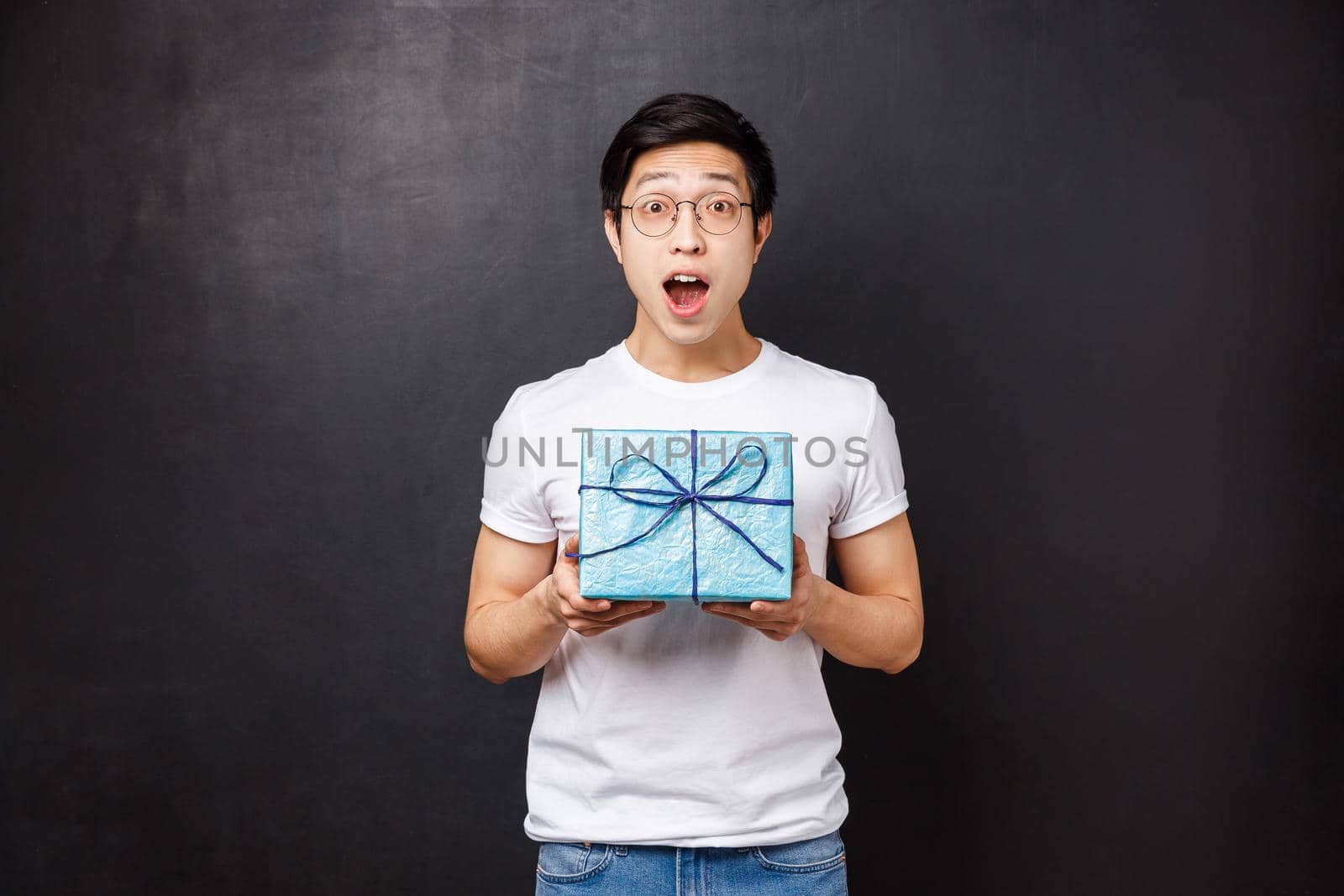 Celebration, holidays and lifestyle concept. Surprised happy young asian b-day guy receive cute wrapped present, holding gift box gasping and looking astonished, celebrating birthday by Benzoix