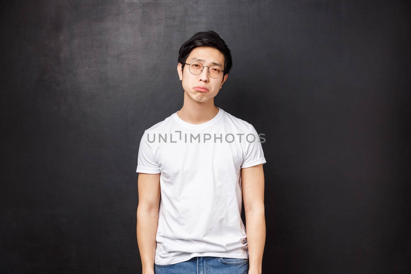 Portrait of gloomy and upset, reluctant tired young male student have lots of homework being drained with duties and part-time job, look fatigue sighing and pouting distressed, black background.