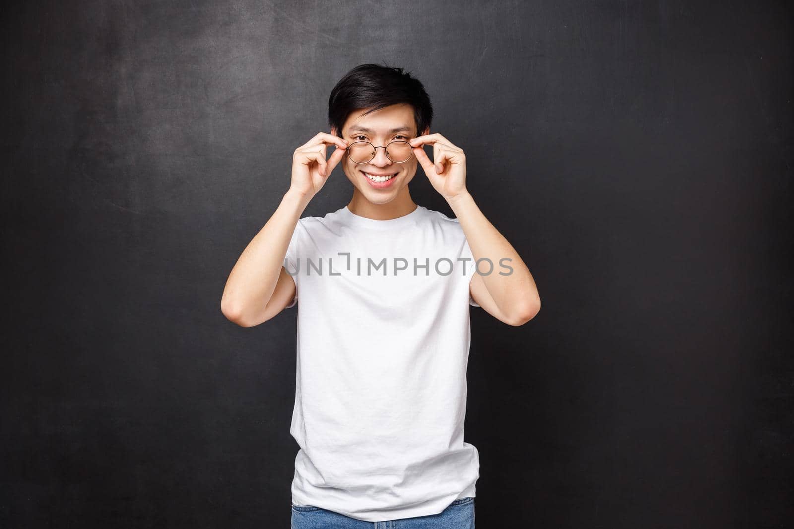 Sassy handsome young asian guy picking new prescribed glasses in optician store, put on eyewear and look confident and pleased camera, smiling white teeth, black background.