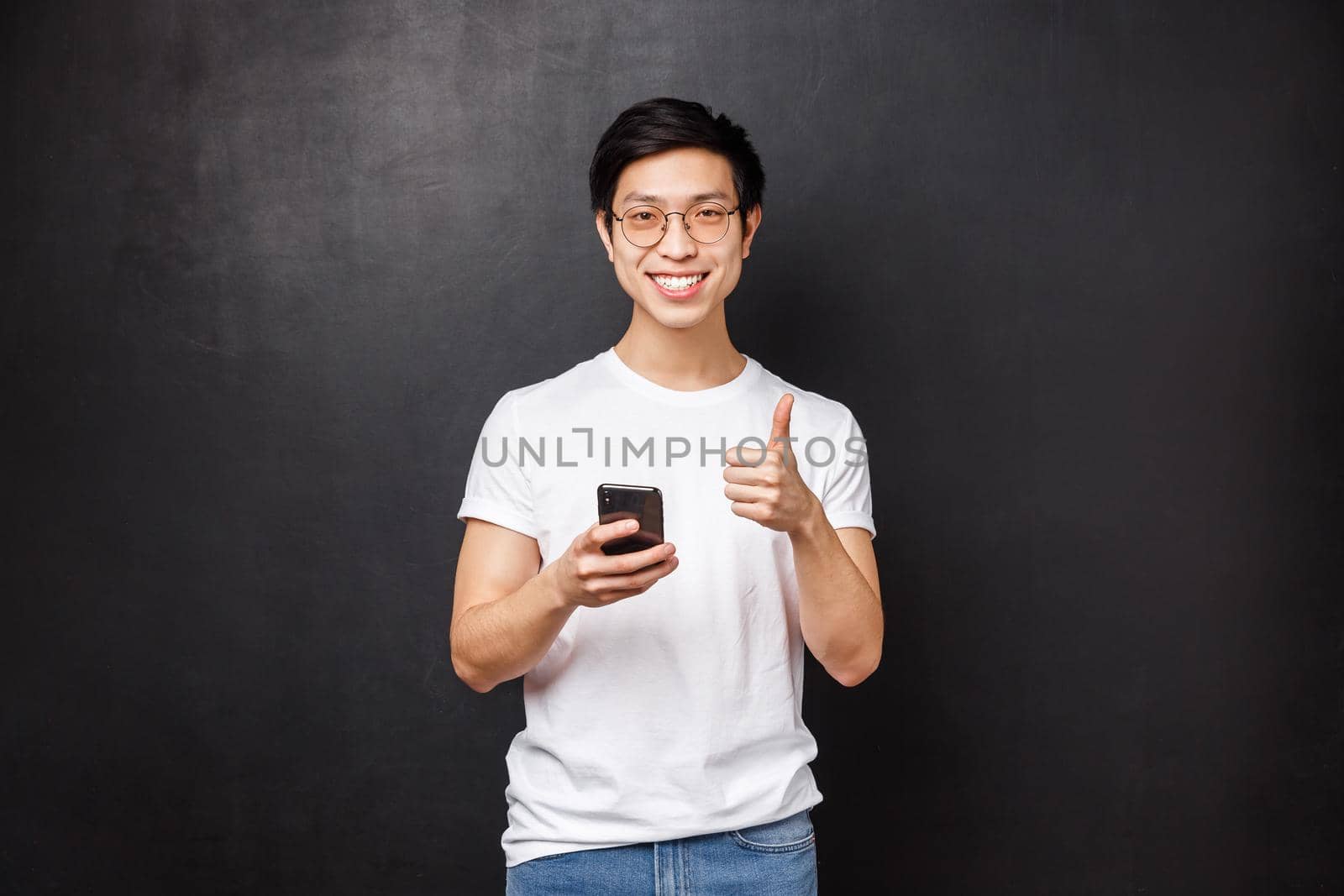 Technology, gadgets and people concept. Satisfied handsome asian guy using mobile phone application, delivery service or internet store, show thumb-up as approve and recommend app.