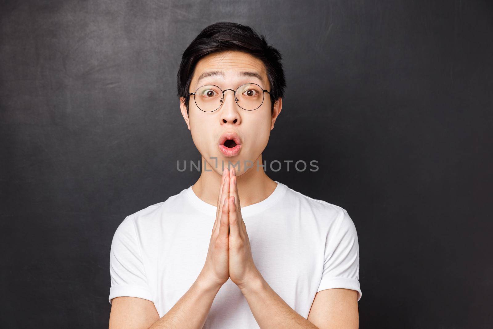 Close-up portrait of amused, enthusiastic young asian man hold hands in pray, clasp palms together as begging for something, asking for help or advice, say please, grateful for friend effort.