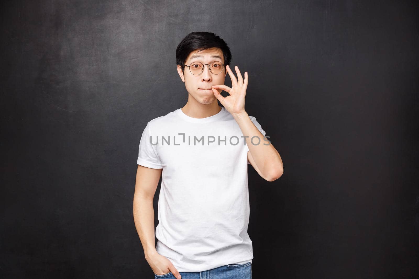 Lifestyle and people concept. Girlfriend share secret with him, cute asian guy promise friend not tell anyone be silent about this conversation, zip lips and look camera, swear, black background.