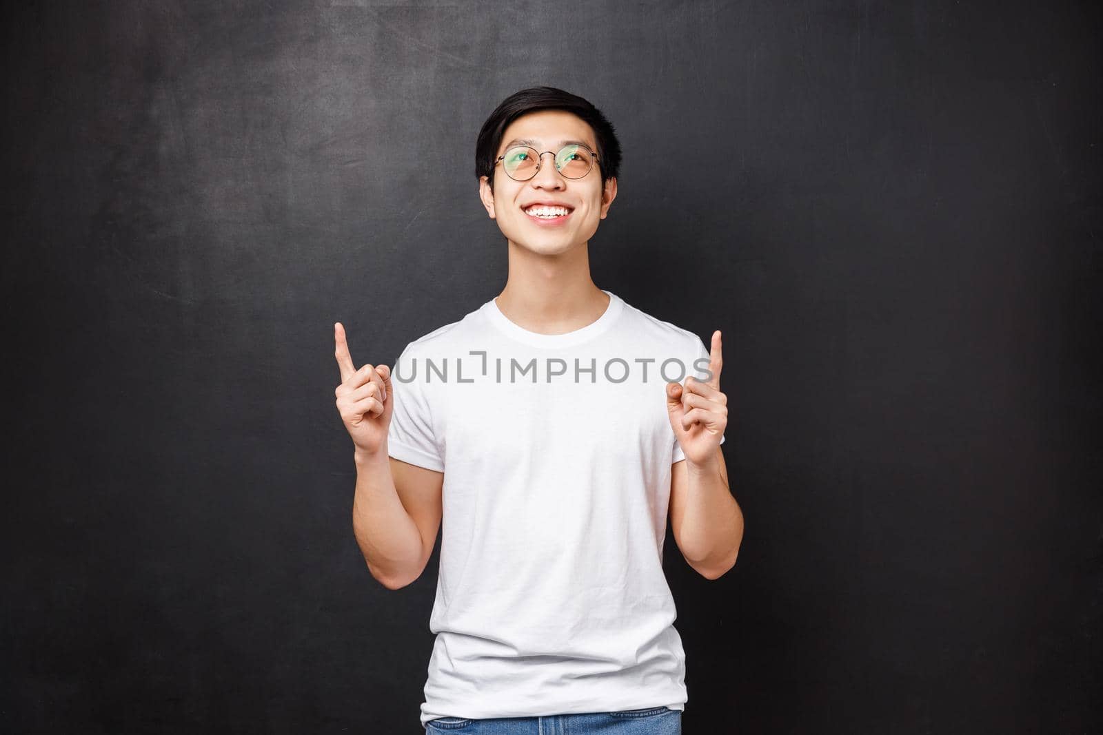 Dreamy happy smiling asian man looking and pointing up, see top advertisement with good deal, decide try himself, contemplating beautiful thing, standing black background by Benzoix
