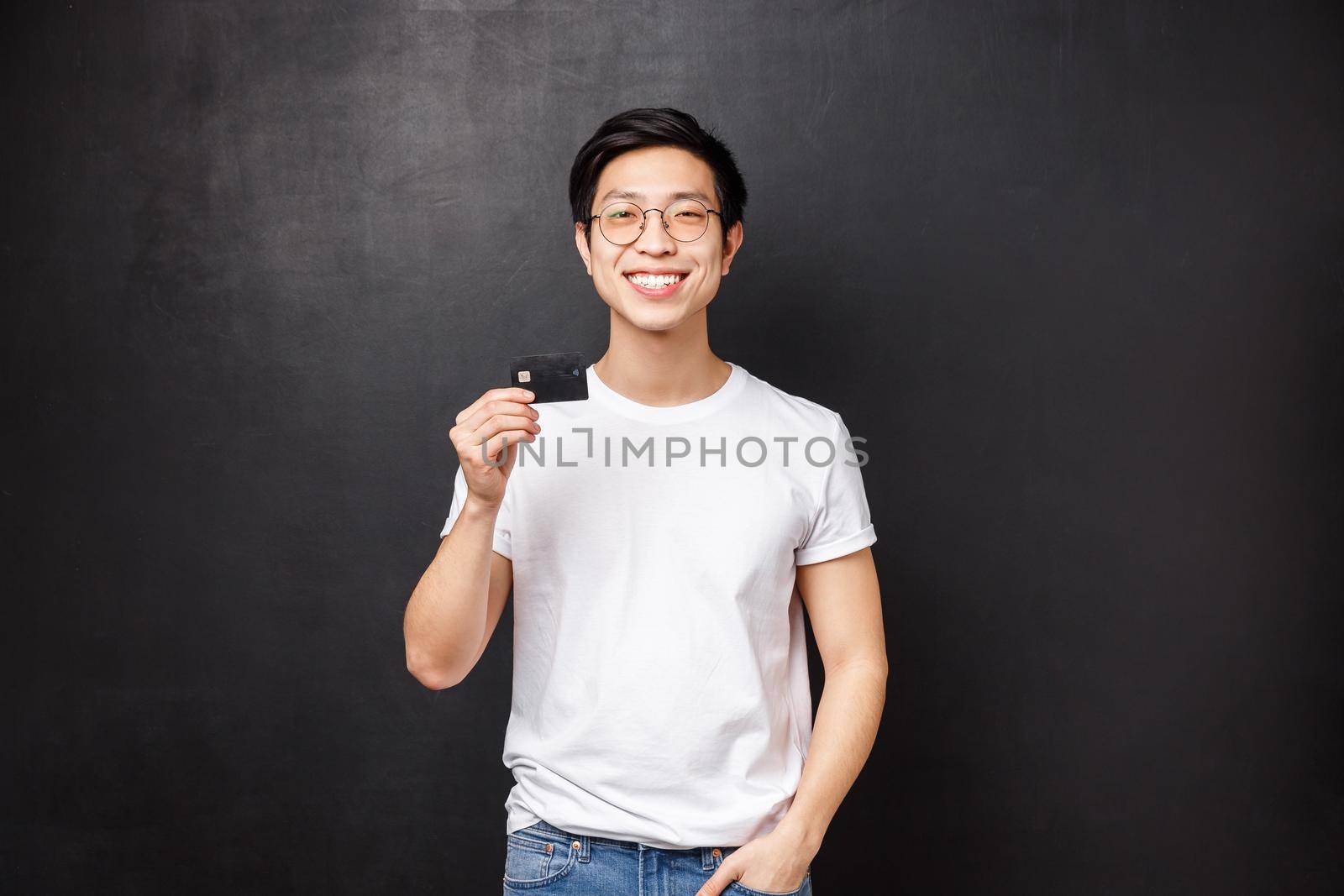 Bank, finance and payment concept. Portrait of satisfied charismatic asian guy in t-shirt and glasses, recommend put money on deposit, pleased with banking service, hold credit card and smiling.