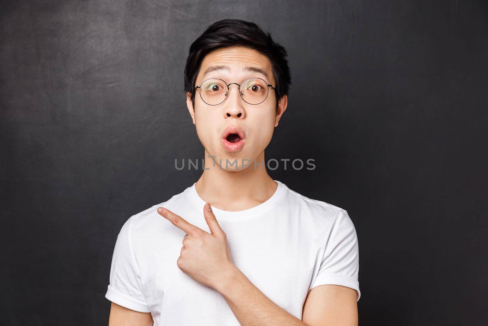 Close-up portrait of interested and surprised, excited young asian guy hear about interesting event going nearby, discuss advertisement with a friend, pointing left and fold lips say wow.