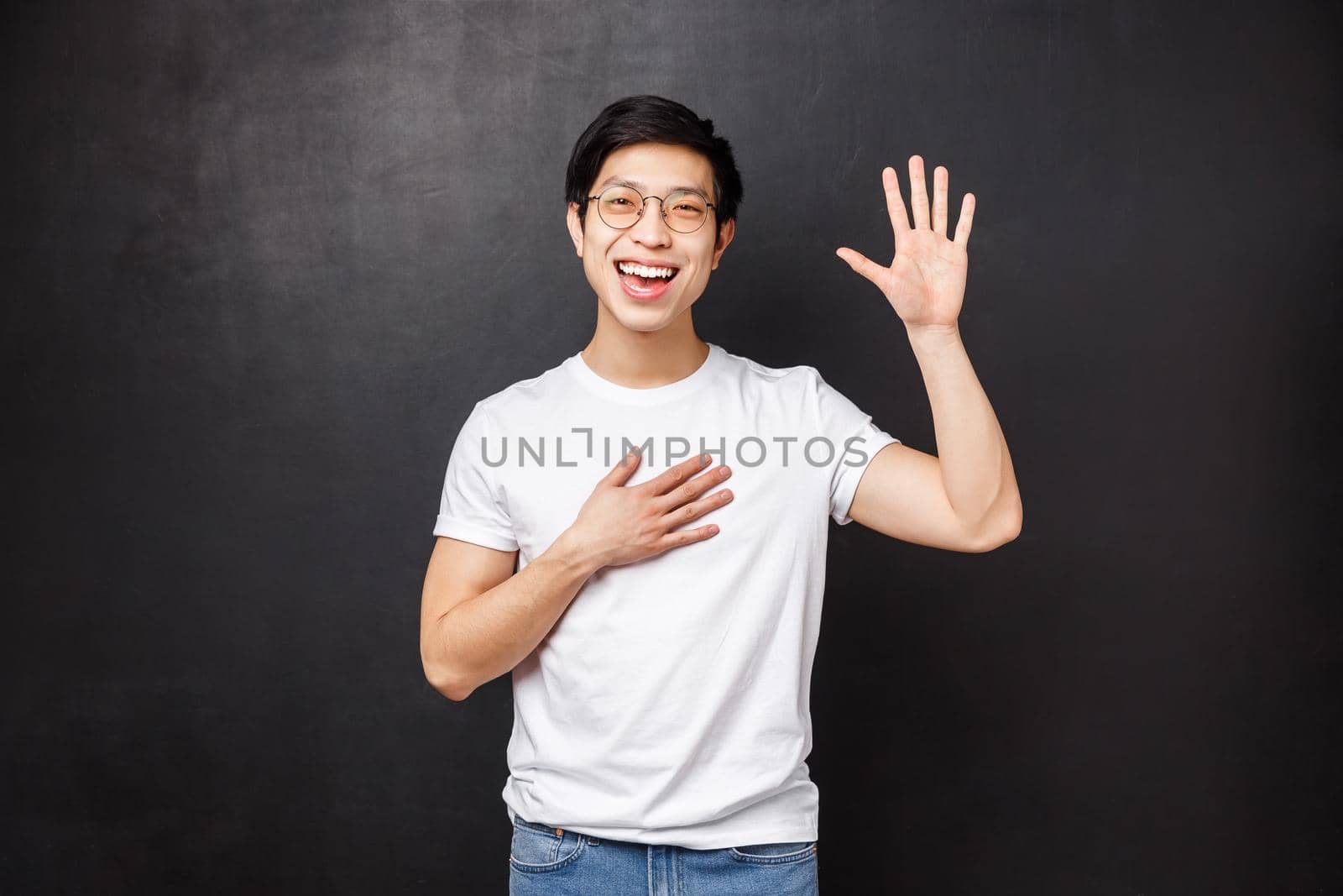 Informal greeting concept. Outgoing attractive young asian guy introduce himself in front of team, raise hand and pointing at him as saying own name, smiling hello gesture, black background.