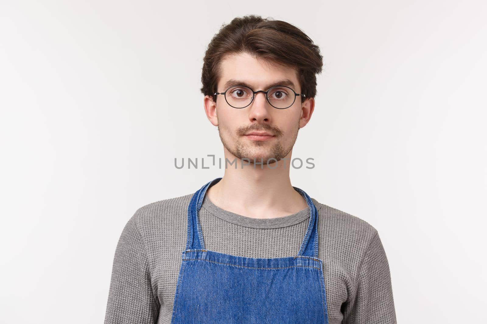 Close-up portrait of caucasian young male student working part-time at coffee shop, start his career in restaurant industry, wearing apron listening to customer order, white background.
