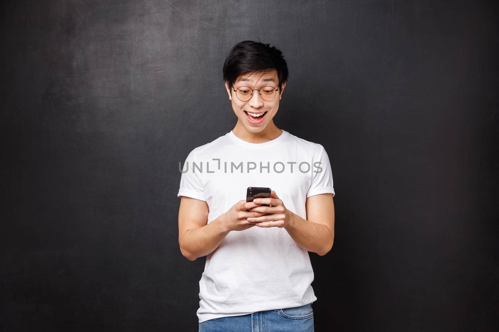 Technology, gadgets and people concept. Happy pleased and excited young asian guy texting girl asking go out with him, feel cheerful and upbeat as she said yes, hold mobile phone.