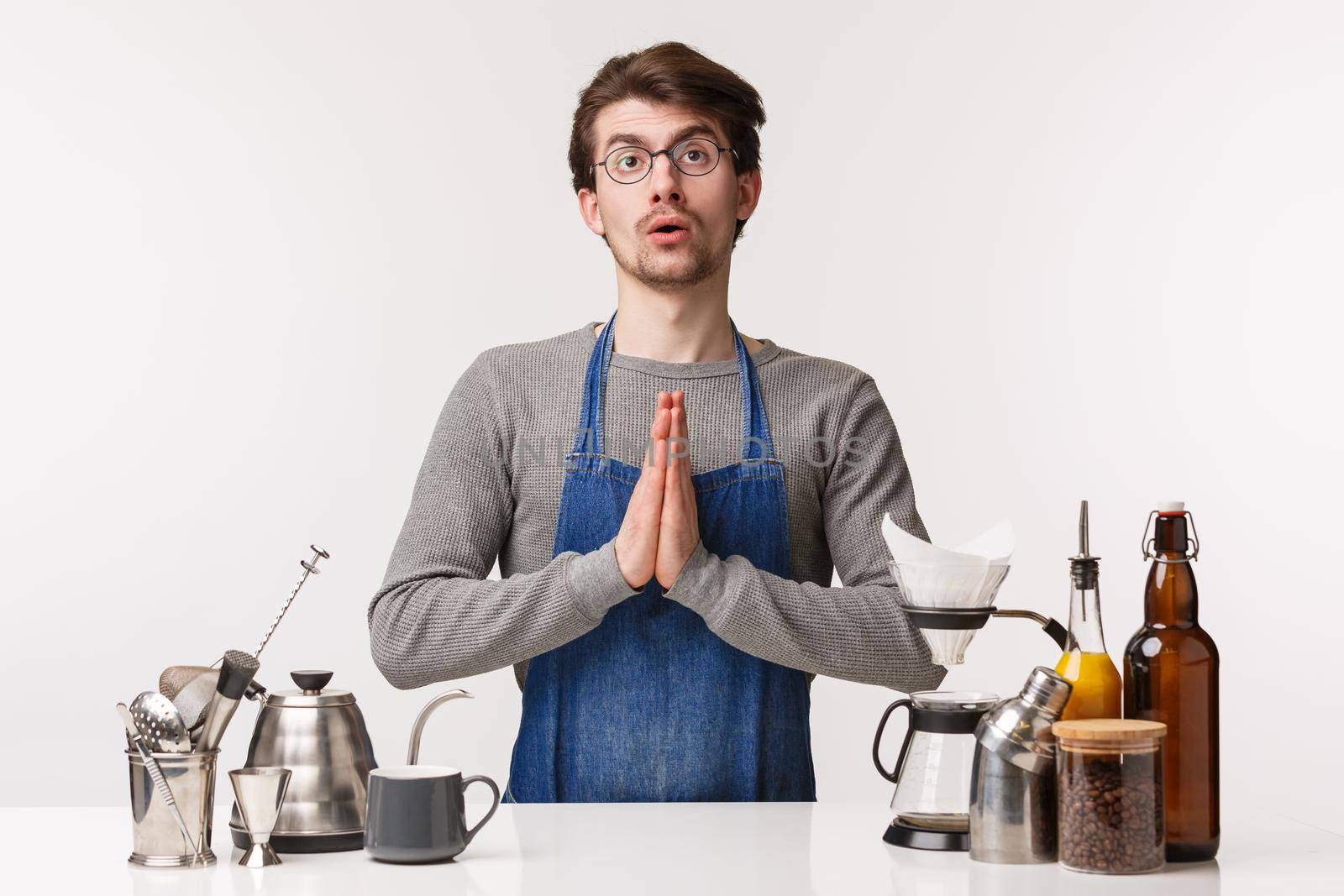 Barista, cafe worker and bartender concept. Portrait of tired cute male employee in apron, praying with distressed expression near bar counter, making coffee, hope client order something simple.