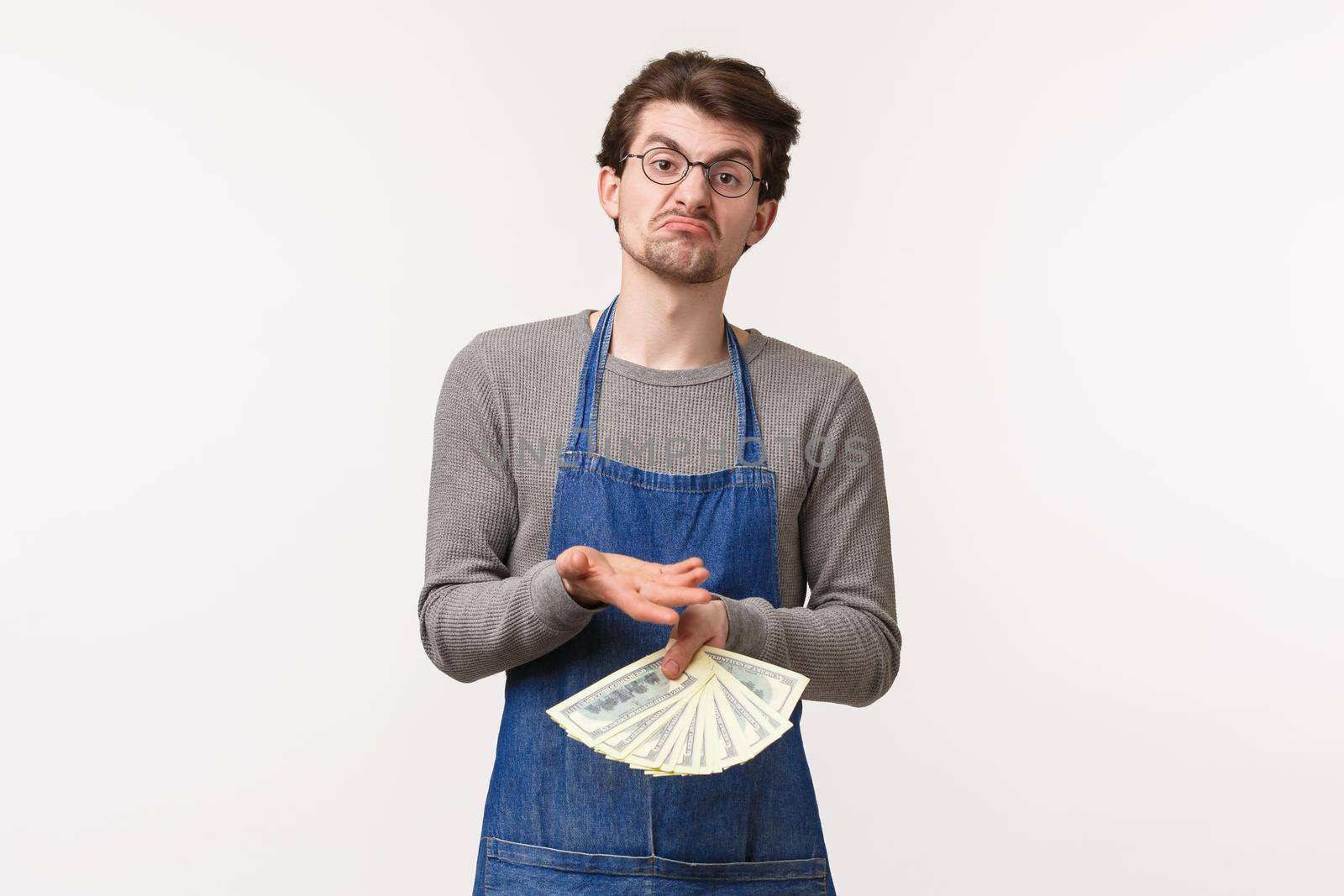 Small business, finance and career concept. Portrait of indecisive and uncertain young male in apron, shrugging and grimacing confused hold money, dont know how to invest cash for profit.