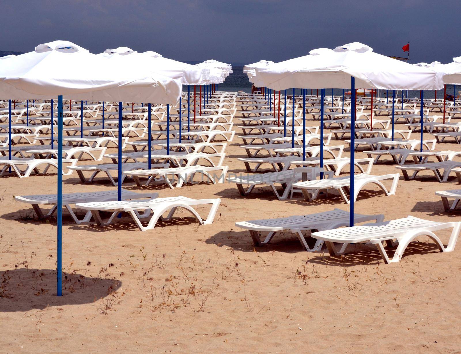 A lot of beach umbrellas and sun beds with a view of a horizon line over the sea on empty beach