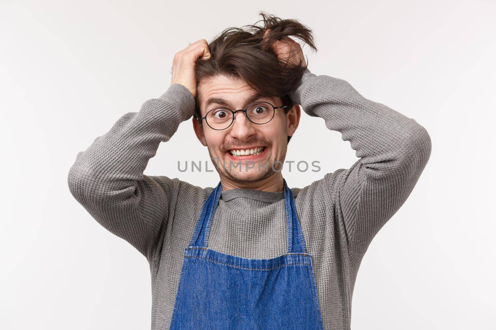 Portrait of distressed and tensed young male barista going insane with lots orders, pulling hair out of head crazy look camera, cant bear stress, feeling disturbed and annoyed, white background.
