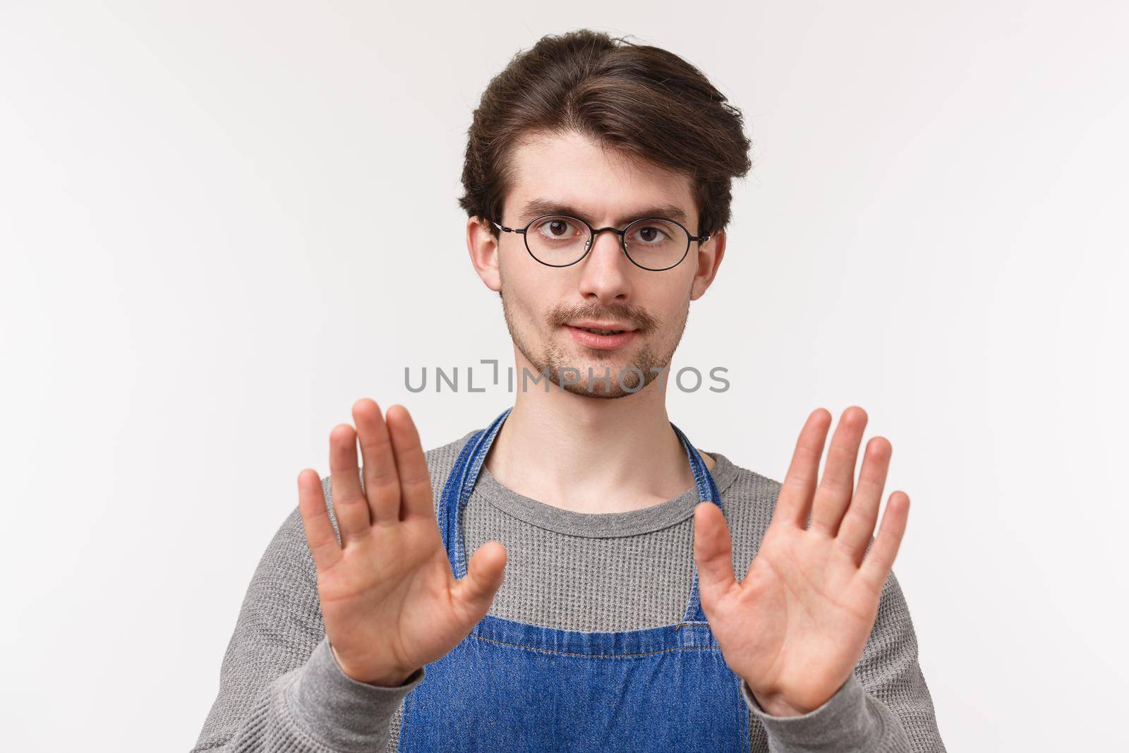 Slow down, take it easy. Close-up portrait of serious-looking confident young male coffee shop manager, employee trying calm person, show stop or easy sign, look camera white background.