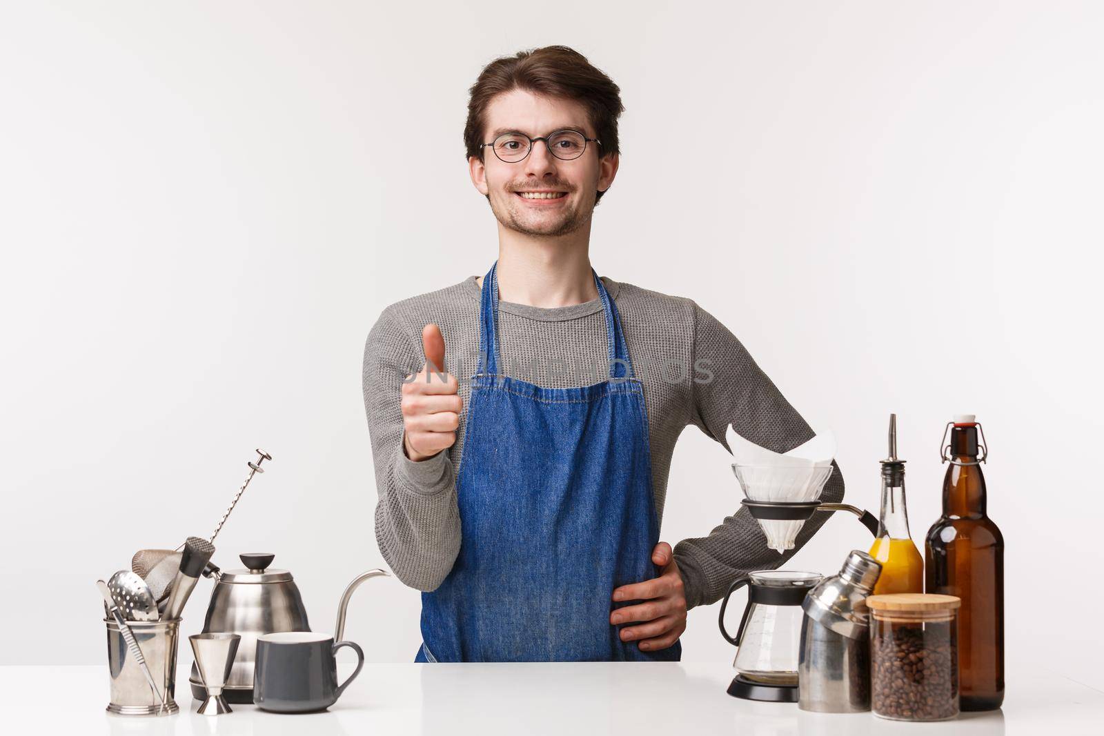 Barista, cafe worker and bartender concept. Portrait of pleased good-looking young man employee in apron, show thumb-up sign and smiling confident, guarantee you will like coffee, approve.