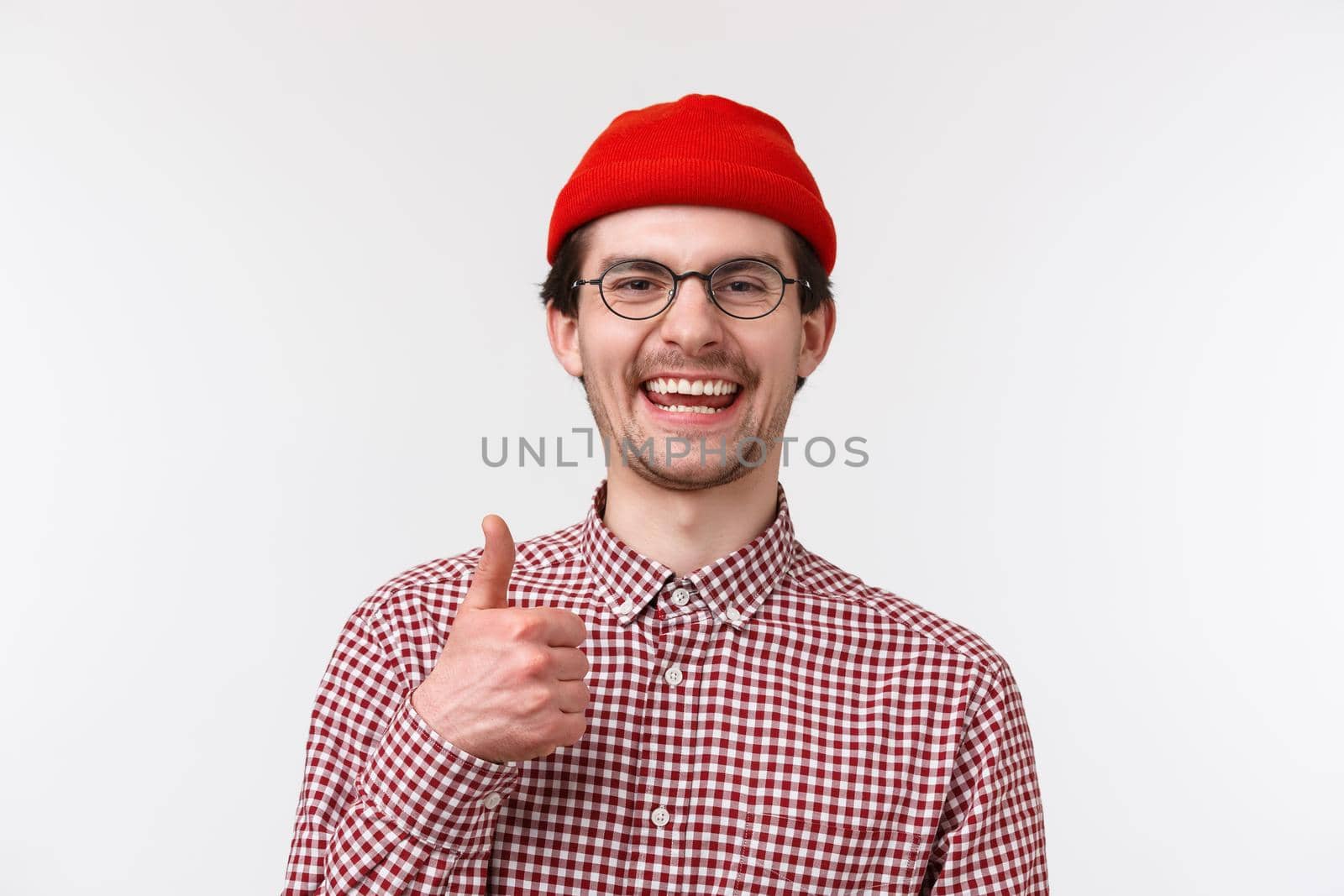 Very good. Satisfied young man approve new product, smiling and laughing pleased, give thumb-up like something really cool, standing white background delighted, agree with you.