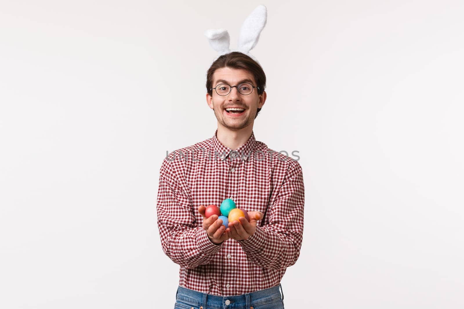 Traditions, religious holidays, celebration concept. Friendly and cheerful cute christian guy, wear rabbit ears, holding painted Easter eggs and smiling joyfully, congratulate with blessing day by Benzoix