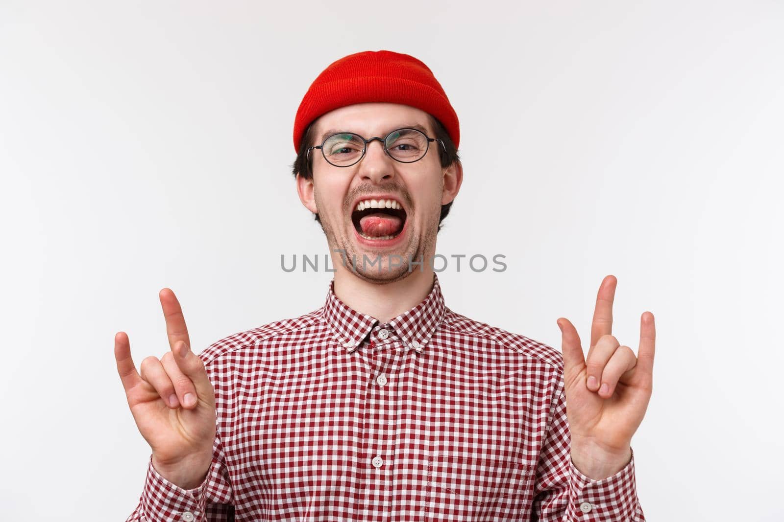 Close-up portrait funny cute bearded young adult guy in red beanie, glasses scream upbeat and excited, showing rock-n-roll, heavy metal gesture enjoying awesome party, standing white background.