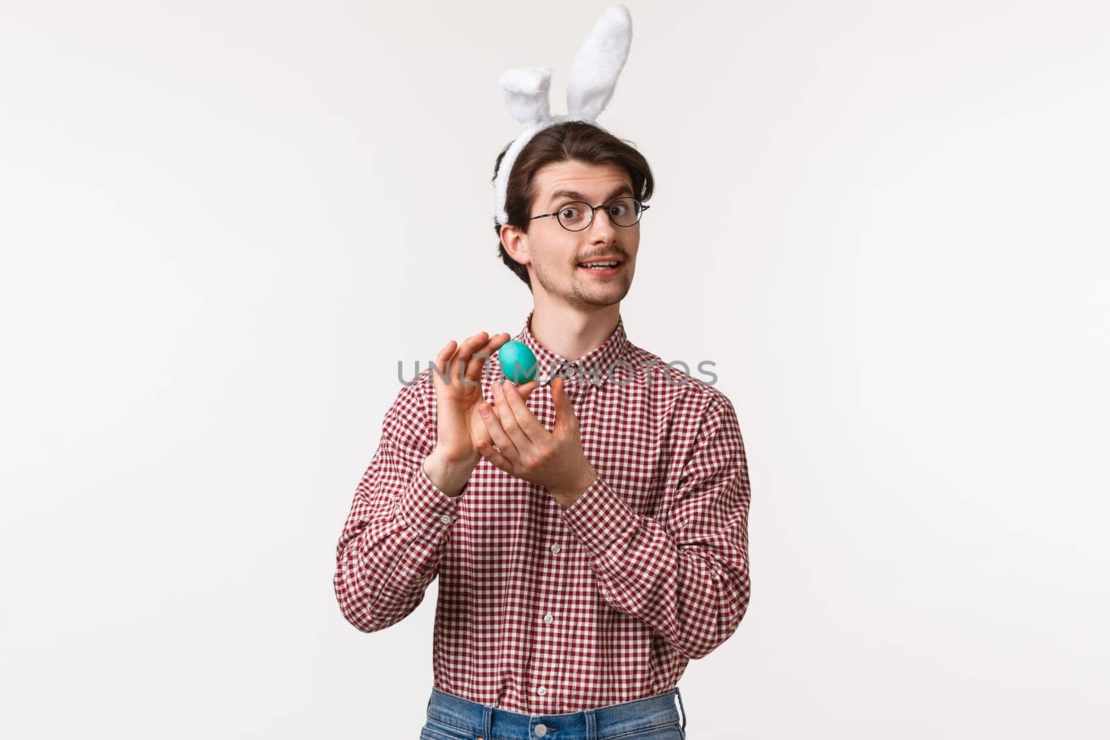 Traditions, religious holidays, celebration concept. Funny and cute bearded guy in glasses and rabbit ears introduce painted egg, prepare for Easter day, feel proud, celebrating with family.