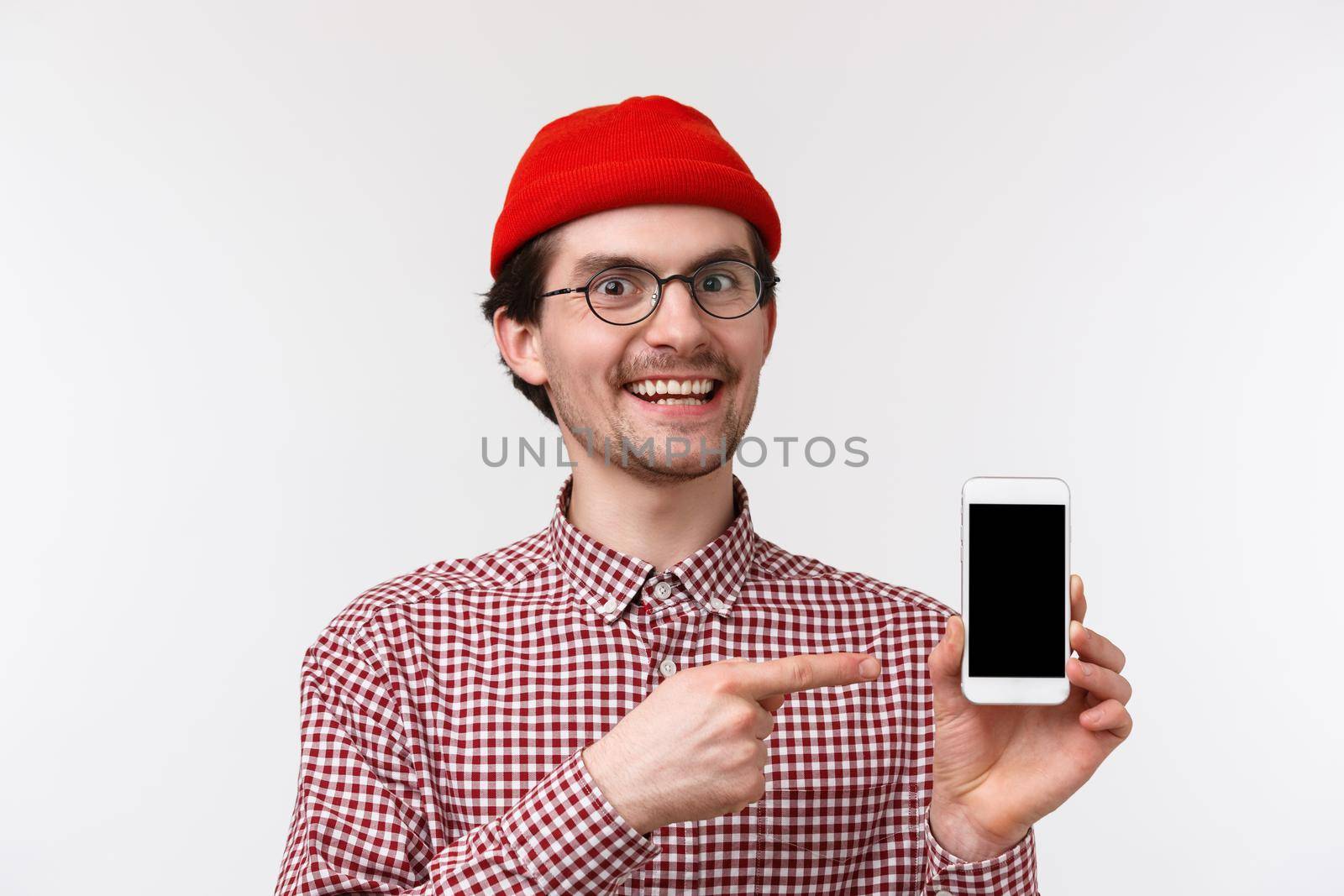 Technology and people concept. Close-up portrait excited pleased young man in red beanie and glasses, recommend subscribe to streaming service or buy app, point mobile phone display, smiling by Benzoix