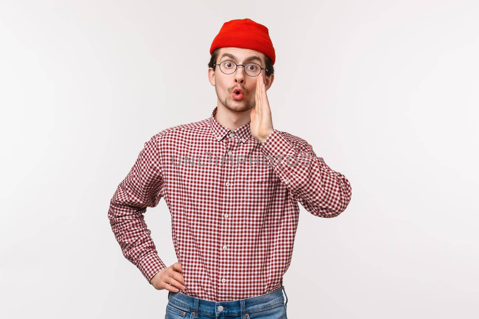 Waist-up portrait of funny young guy with beard and moustache in red beanie, glasses, calling someone, searching for friend in crowd, hold hands near mouth gossiping, whisper secret by Benzoix