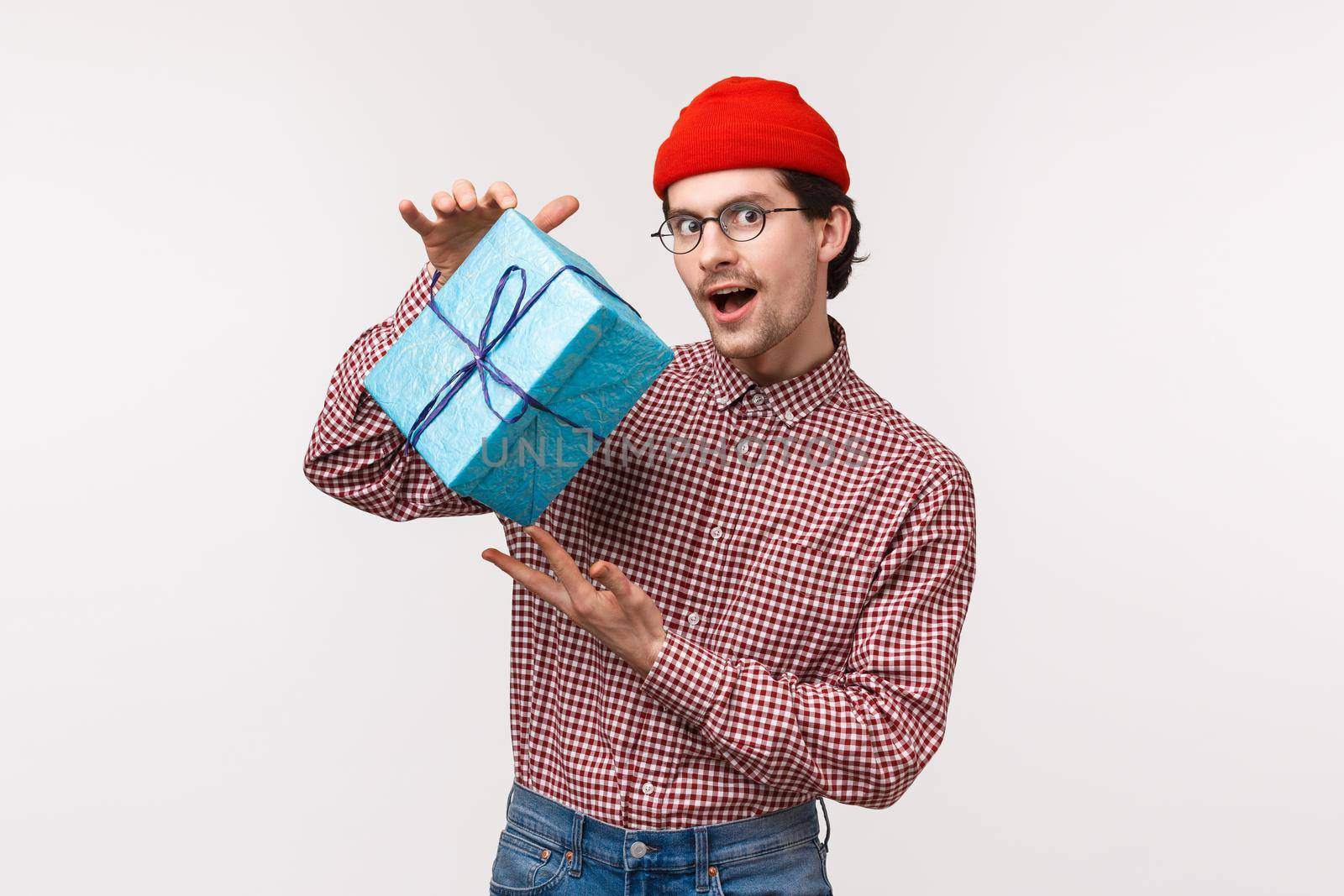Guy trying make intrigue as prepared present for girlfriend, shaking wrapped box with gift, wonder whats inside, look mysterious and cunning camera, wear red beanie checked shirt, white background by Benzoix