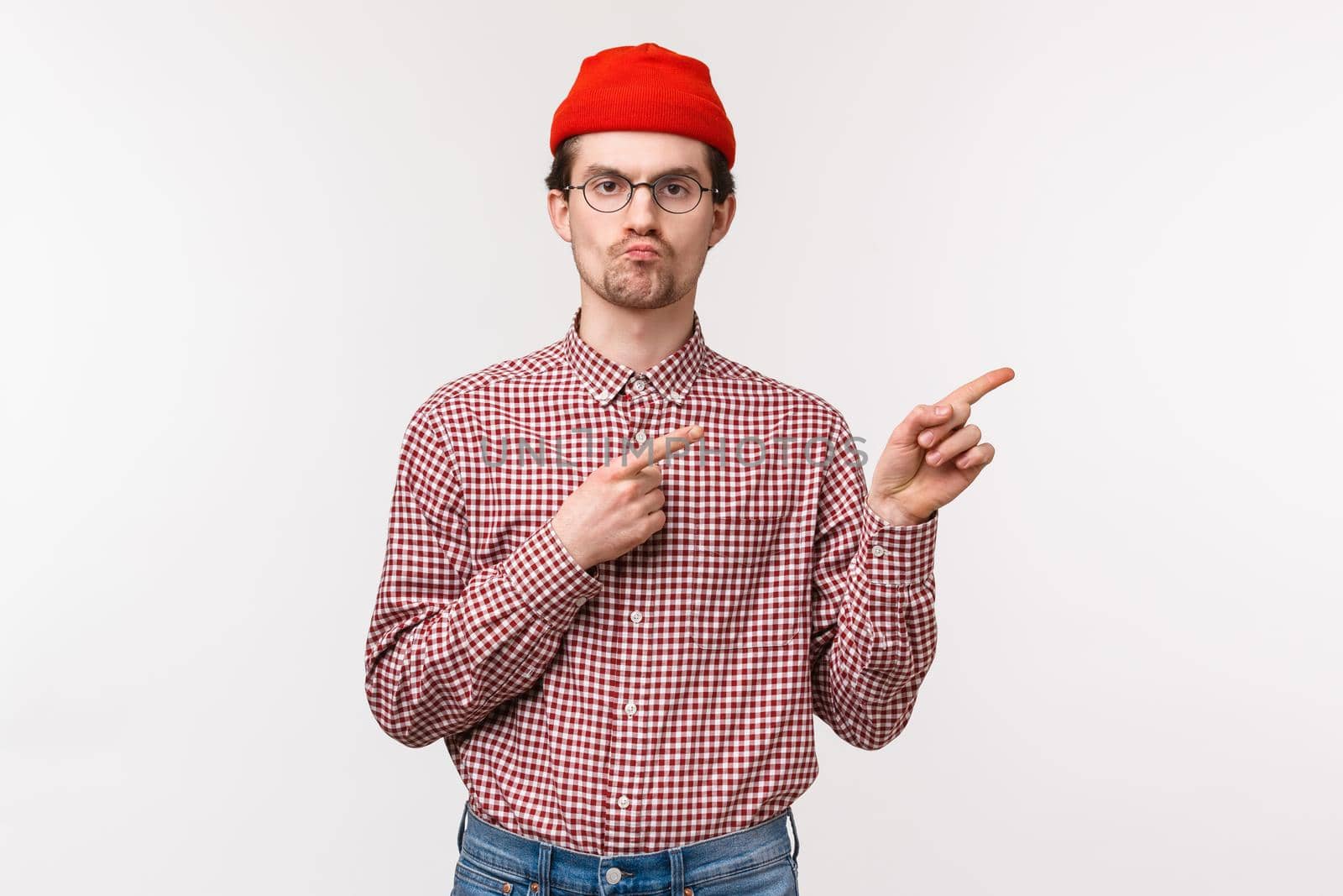 Skeptical serious-looking bothered young geeky man in red beanie and glasses, pouting with unsatisfied grimace pointing upper right corner, annoyed seeing something awful, express dislike by Benzoix