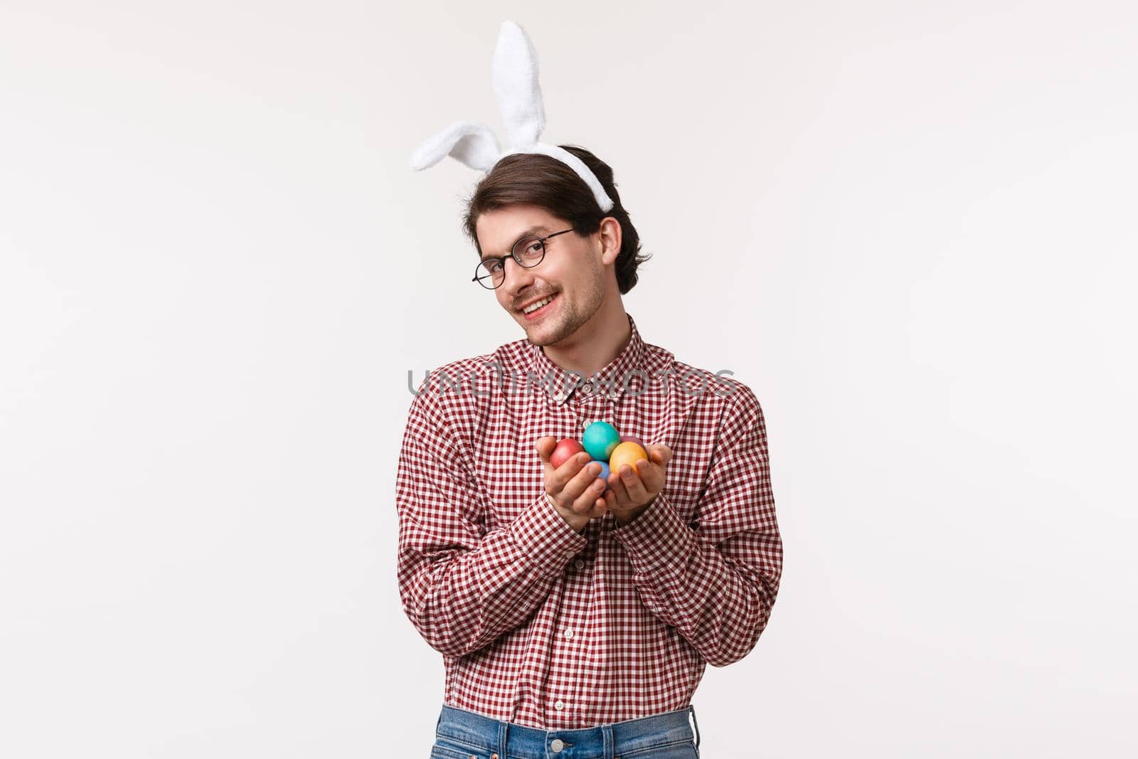 Traditions, religious holidays, celebration concept. Silly and cute, lovely boyfriend celebrating holy Easter day, coquettish looking with pleased smile, wear rabbit ears, holding painted eggs.