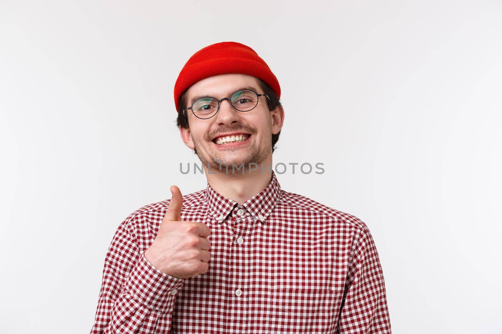 Close-up portrait satisfied smiling young bearded man, show thumb-up in approval or accepting gesture, nod agreement, recommend something really good, place worth visit, stand white background.