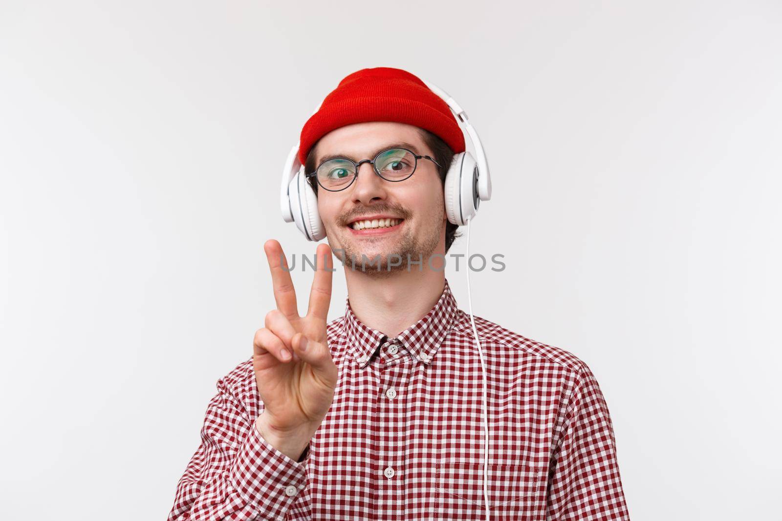 Music, technology and people concept. Peace dudes. Cheerful cute hipster man in glasses and check shirt, wear glasses listening music in headphones stay positive, smile and show goodwill sign.