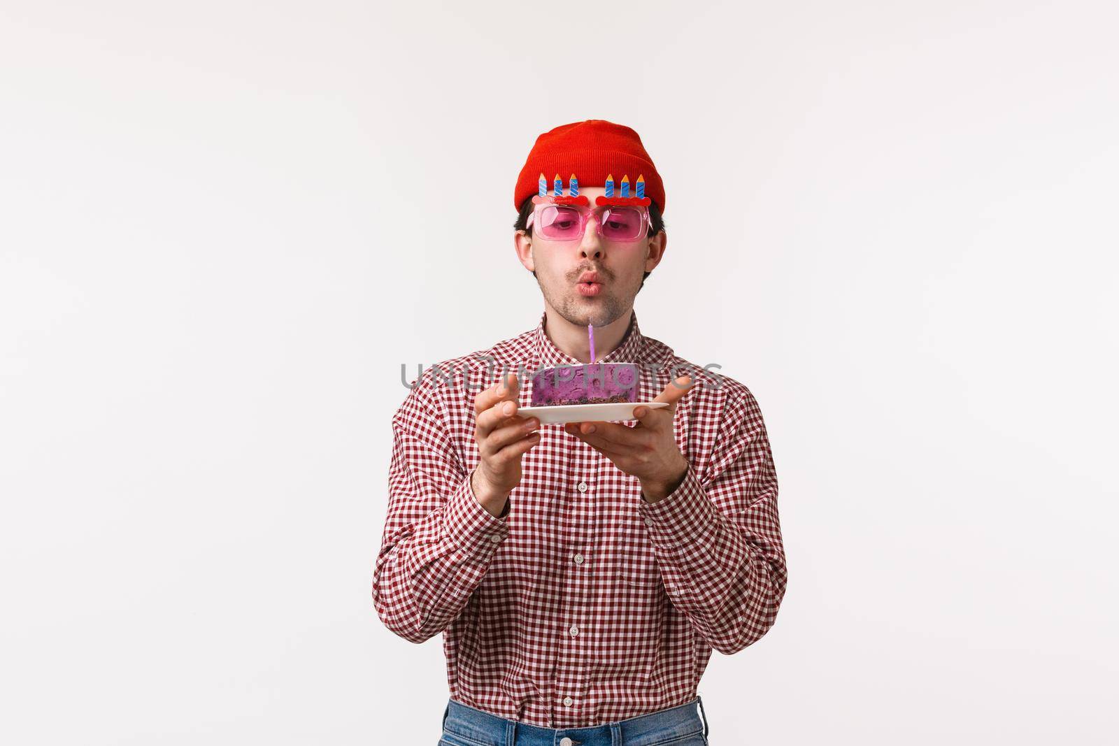 Celebration, holidays and lifestyle concept. Cute adult caucasian man celebrating his birthday in funny sunglasses, friends throw party, sing song as he blow out candle on b-day cake by Benzoix