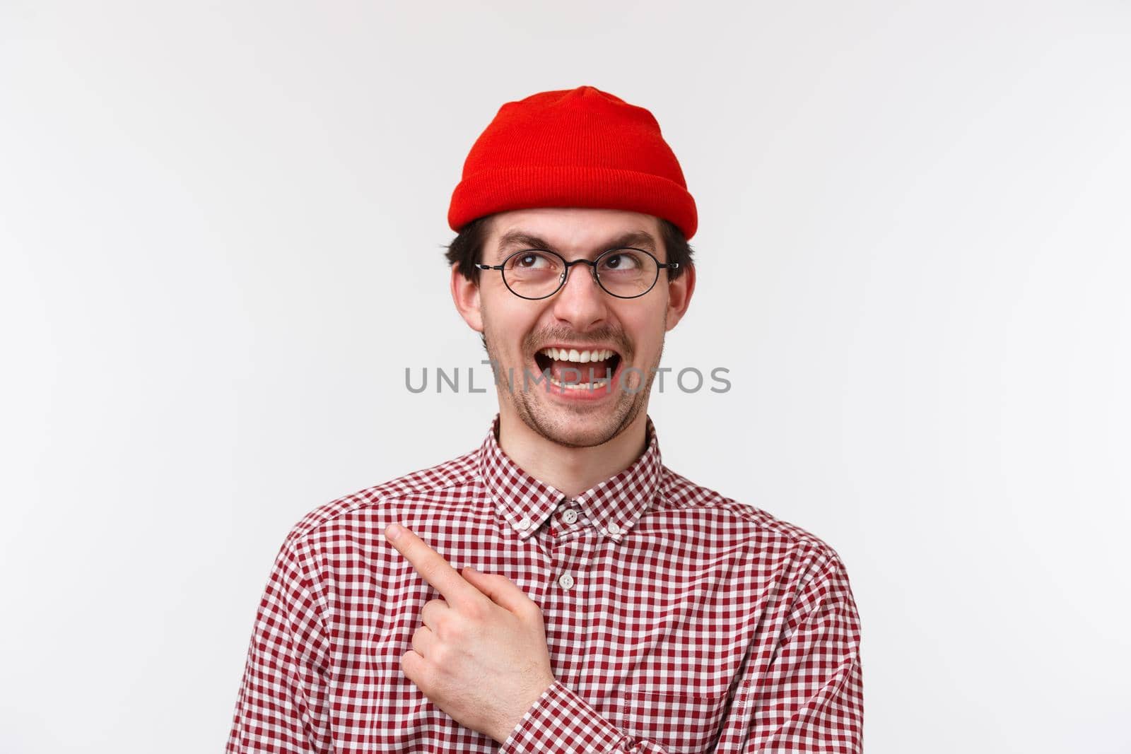 Guy approves the choice. Happy and smiling caucasian male in red beanie and glasses pointing to upper left corner, white background. by Benzoix
