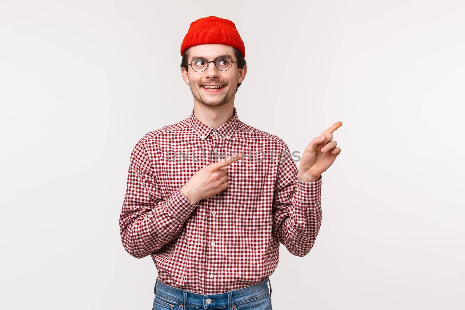 Waist-up portrait of curious excite geeky adult man in red beanie, checked shirt, pointing and looking upper right corner with intrigued enthusiastic smile, foundsomething interesting.