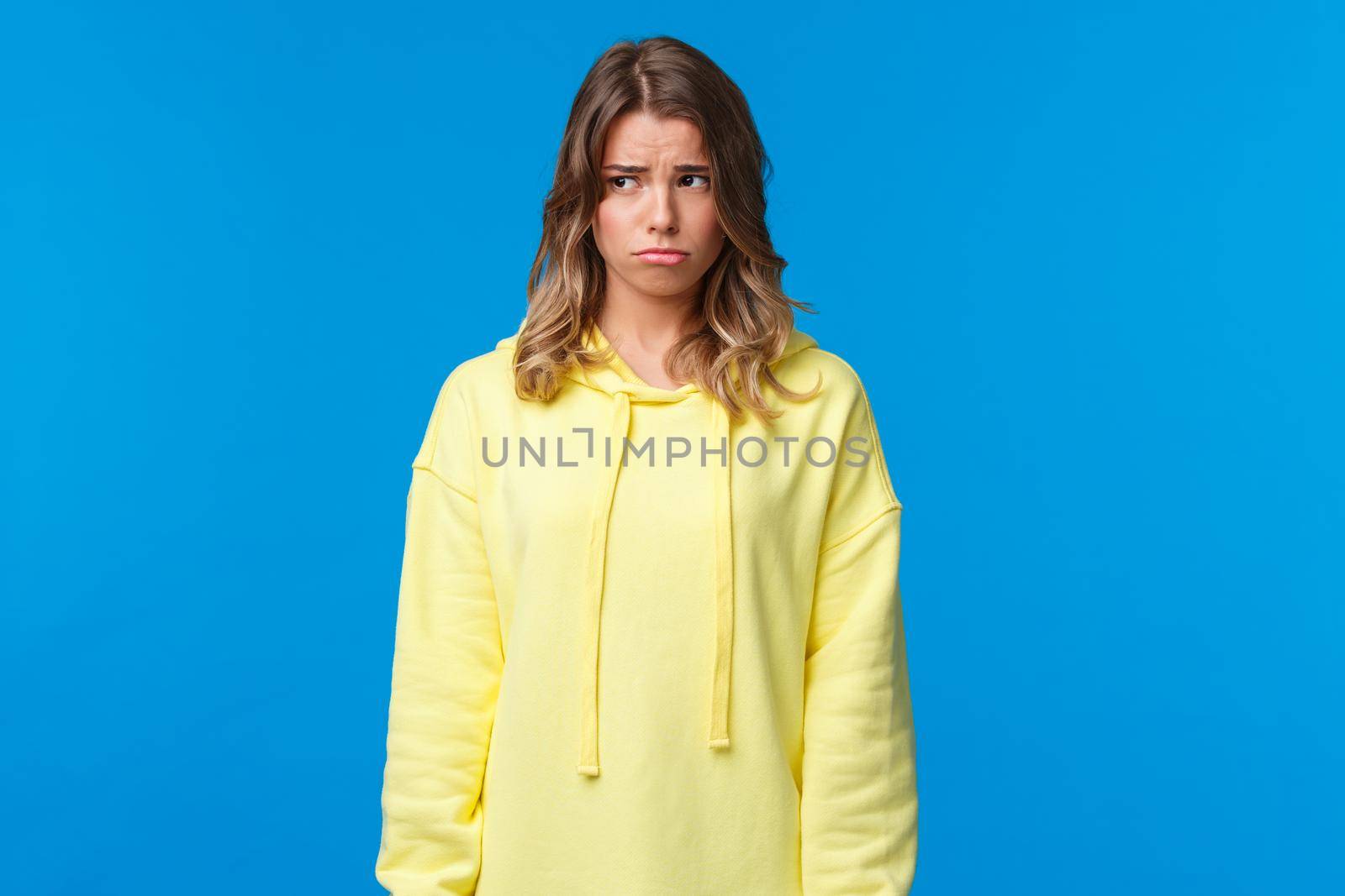Gloomy and lonely say caucasian girl looking away, sobbing childish and sulking as feeling uneasy, being let down, having bad day at university, standing upset over blue background.