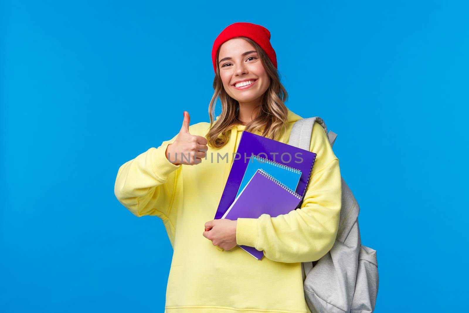 Sounds good. Cheerful cute and smart caucasian girl in red beanie studying hard for exams, encourage student keep up, show thumbs-up in like or approval, hold notebook and backpack by Benzoix