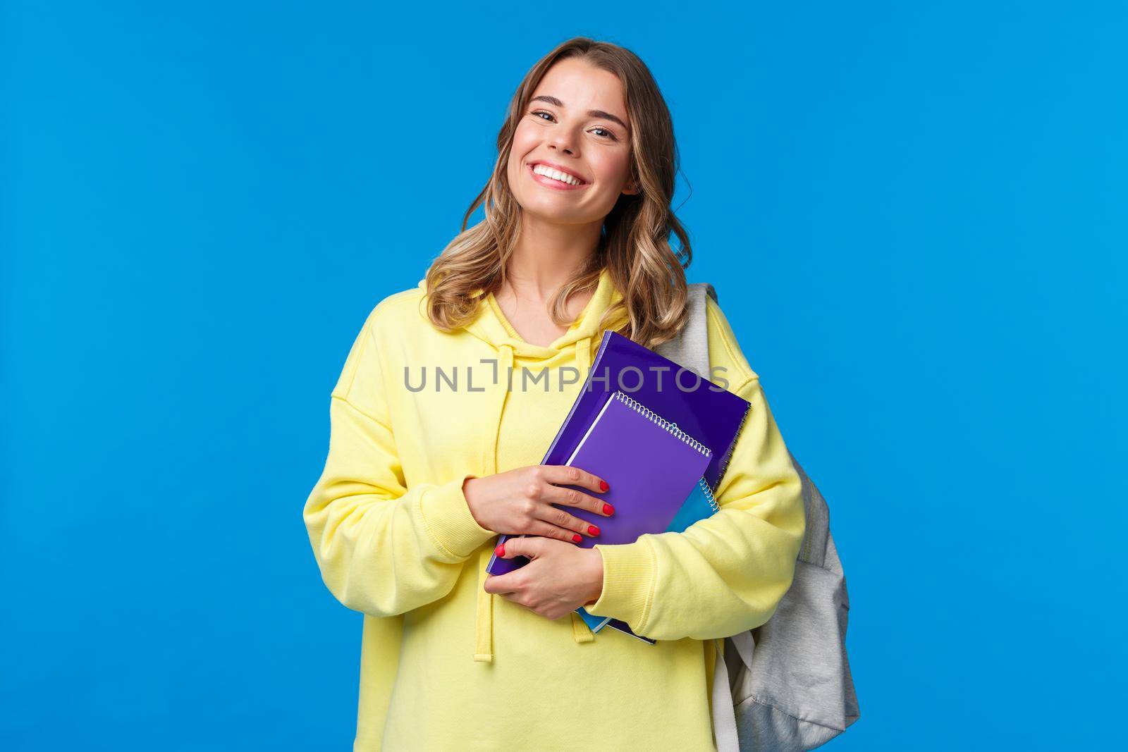 Charismatic joyful european female carry backpack and notebooks as going next lecture, smiling happy, enjoying student lifestyle, studying in university, standing blue background by Benzoix