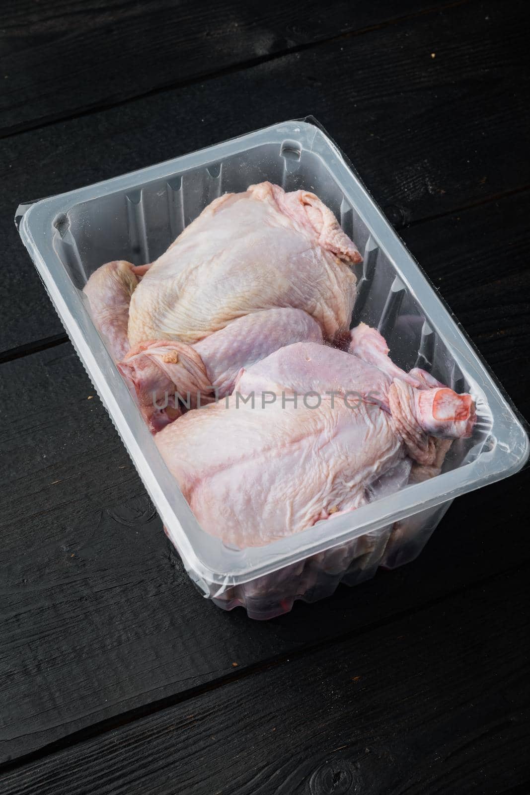 Plastic container with raw chicken set, on black wooden table