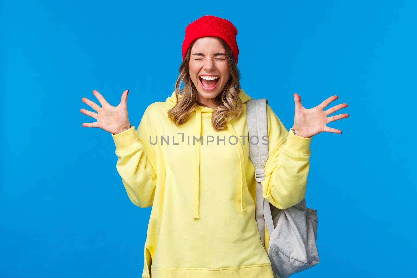 Carefree happy girl relieved finally classes are over and summer vacation starting, screaming from joy and positive emotions with closed eyes shaking hands happily, carry backpack.