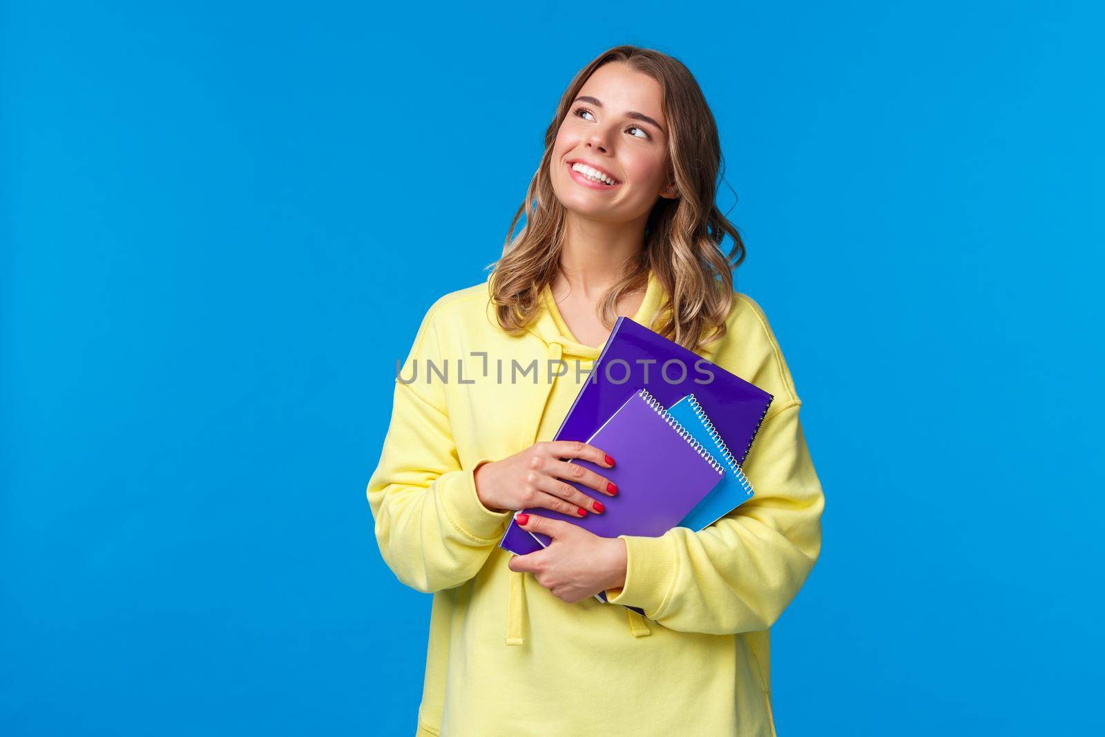 Back to school. Cute blond smiling european female student carry notebooks and learning material, look dreamy upper left corner smiling, thinking what she grab for lunch, blue background by Benzoix